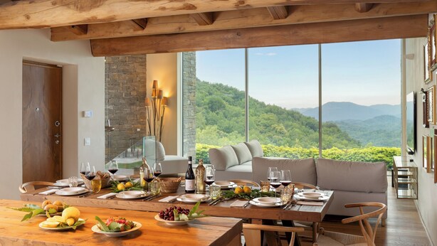 A dining area with a table set for a meal, a sofa, and a view of a mountainous landscape.