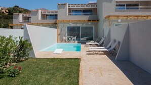 A modern building with a swimming pool, lounge chairs, and a small table with chairs.