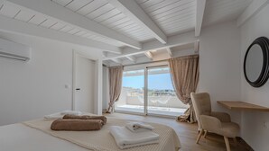 A hotel room with a large bed, a chair, a small table, and a balcony with a view.