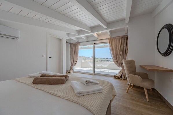 A hotel room with a large bed, a chair, a small table, and a balcony with a view.