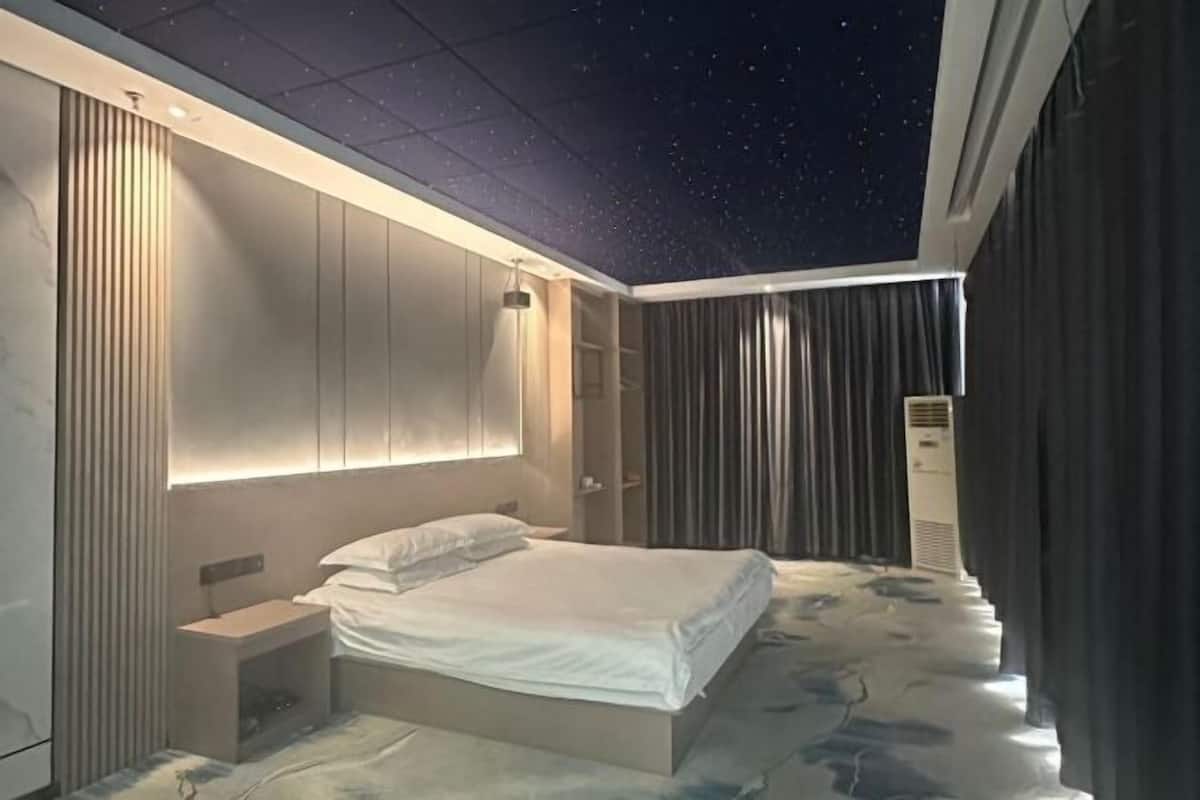 A modern hotel room with a starry ceiling, a bed, a bedside table, and a window with curtains.