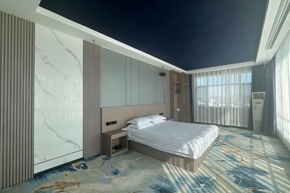 Una habitación de hotel moderna con cama, mesita de noche y un gran ventanal con cortinas.