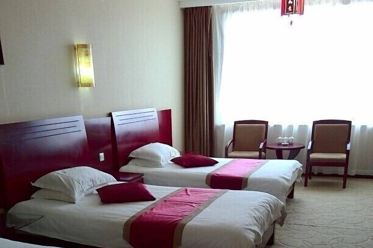 A hotel room with four beds, each with white linens and red accents, a small round table, and a chair.