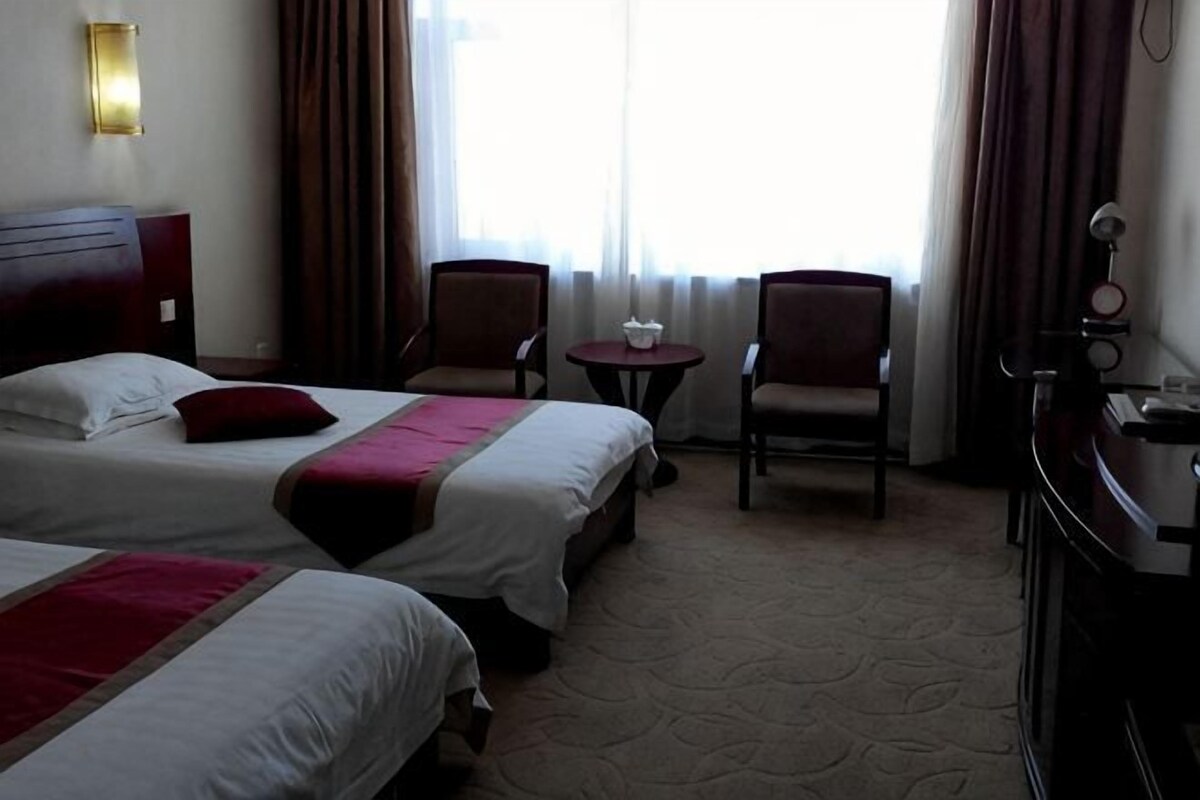Quarto de hotel com duas camas, uma escrivaninha, uma cadeira e uma mesa pequena.