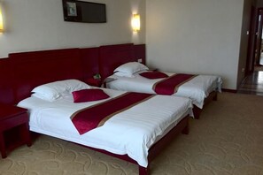 A hotel room with two beds, each with white linens and red accents, a wooden headboard, bedside tables, and wall-mounted lamps. - Shang Yuan Hotel (Habahe)
