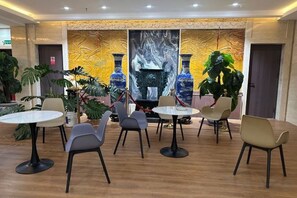 Un comedor con mesas y sillas redondas, un gran muro decorativo y plantas en macetas.