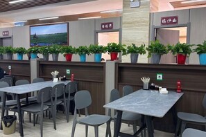 A restaurant with multiple tables and chairs, potted plants, and a television screen on the wall. - Shang Yuan Hotel (Habahe)