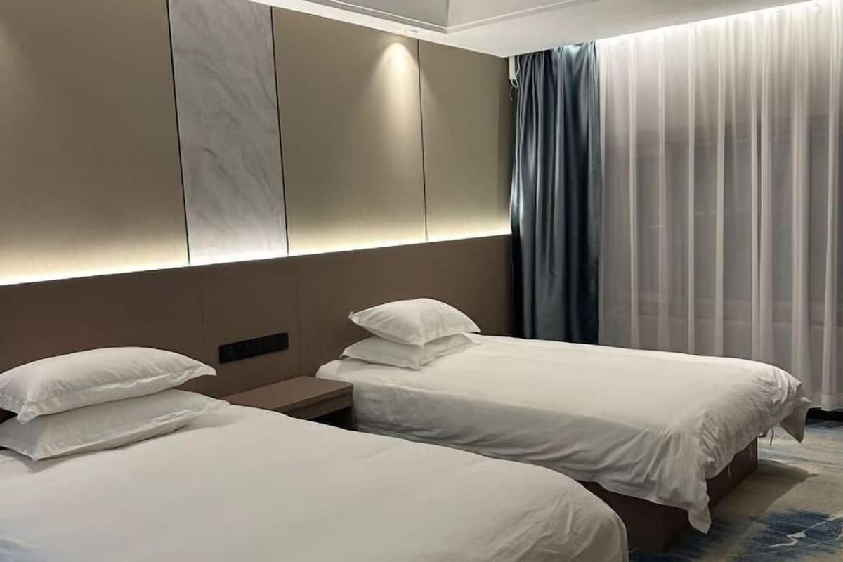 A hotel room with two beds, a large window with curtains, and a wall with a built-in light panel.