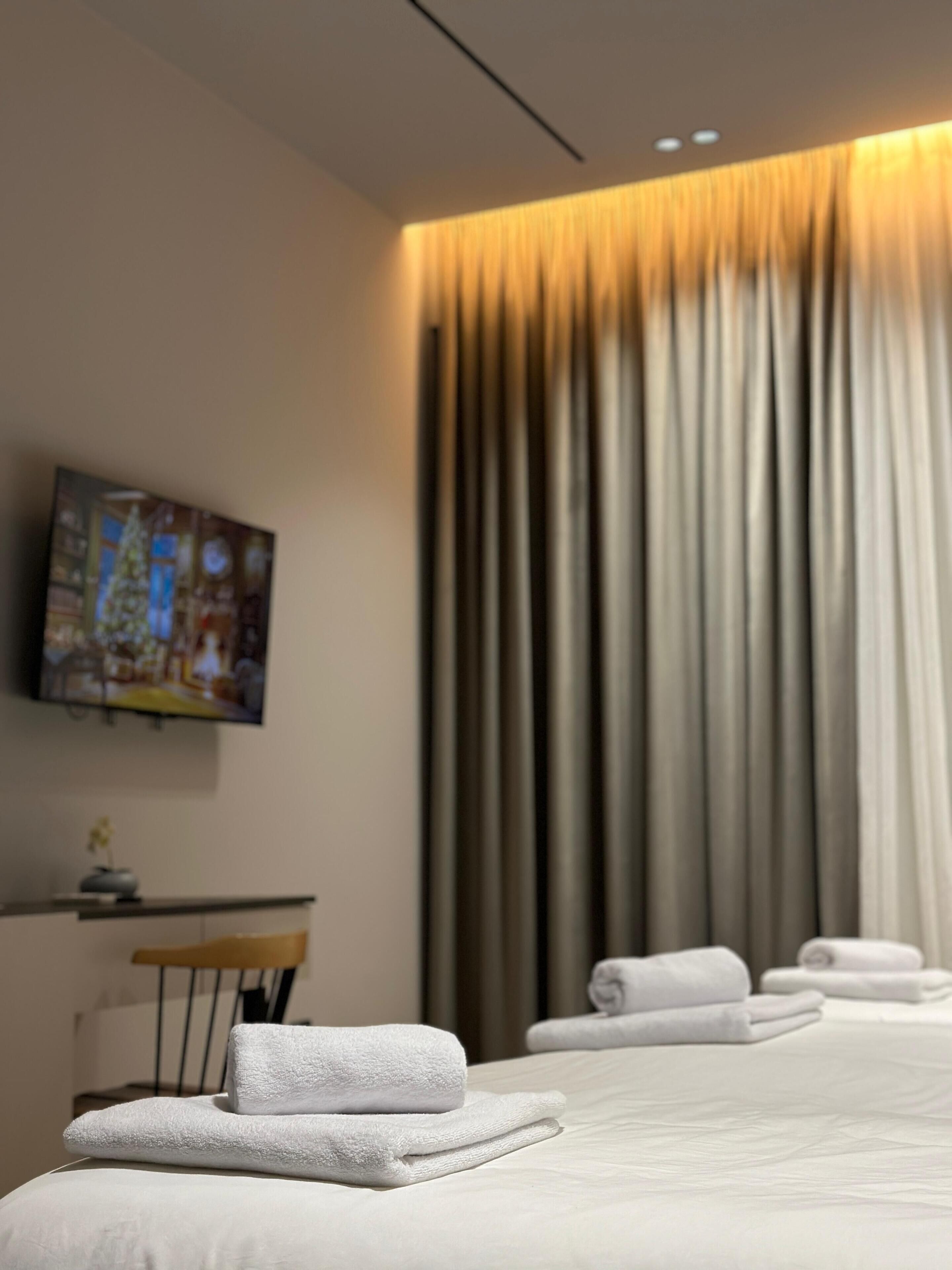 Une chambre d’hôtel avec un lit, un téléviseur à écran plat fixé au mur et une grande fenêtre avec des rideaux.