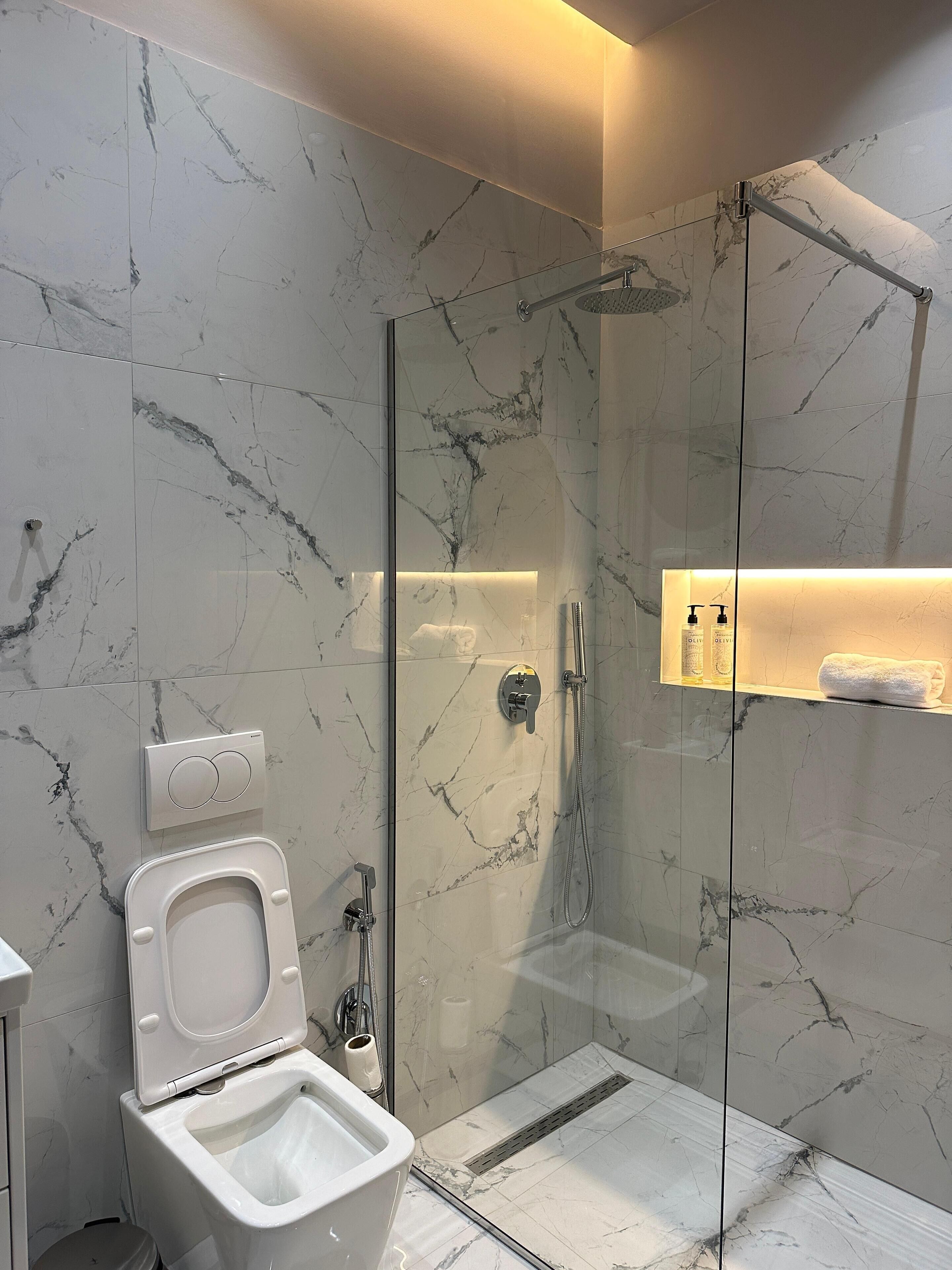 Un baño moderno con ducha envuelta en vidrio, un bidé y paredes de mármol.