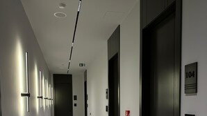 Ein moderner Flur mit Holzboden, einer Reihe von Wandleuchten und einer Tür mit einer Nummer, die Zimmer 104 anzeigt.