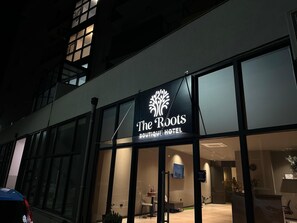Una entrada de hotel moderna con un gran letrero iluminado que dice 'The Roots Boutique Hotel'.