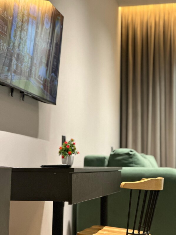 A modern living room with a flat-screen TV mounted on the wall, a small table with a vase of flowers, and a green sofa.