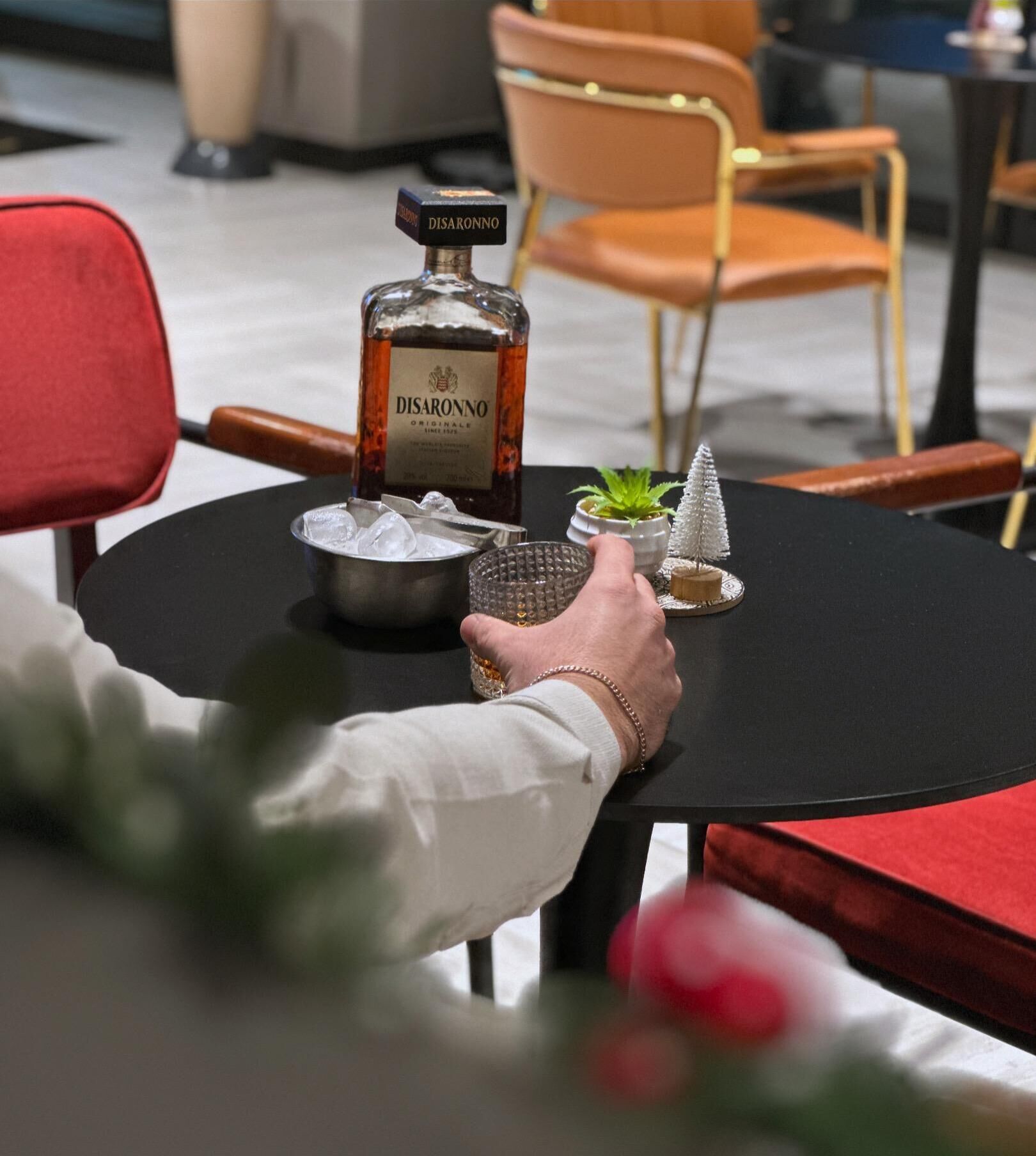 Una botella de Disaronno sobre una mesa con hielo, una planta pequeña y un adorno.