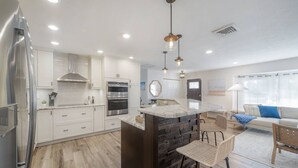 A modern kitchen with white cabinets, a central island, and a dining area with a bar stool.