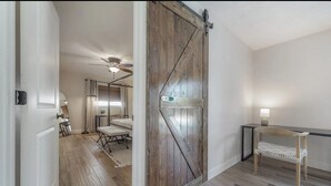 A room with a wooden floor, a bed, a desk with a chair, and a sliding barn door.