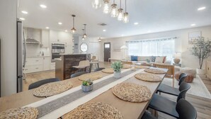 A modern kitchen with white cabinets, a built-in oven, and a dining area with a long table and woven placemats.