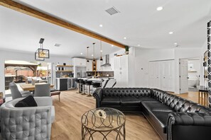 A modern living room with a sectional sofa, a glass coffee table, and a dining area with bar stools. - Golden Paradise POOL SPA FUN (Downey)
