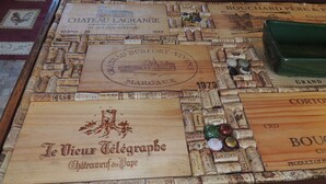 Un juego de mesa de madera con tapones y etiquetas de vino antiguos, incluyendo Chateau Lagrange y Bouchard Père & Fils.
