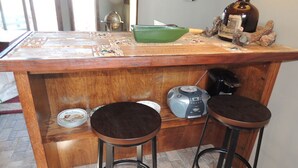 Una zona de bar con barra de madera, dos taburetes, una balanza, una radio y un bol verde sobre la encimera.