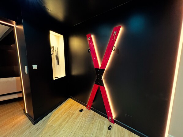 A modern interior with a wooden floor, a black wall, and a red X-shaped light fixture.