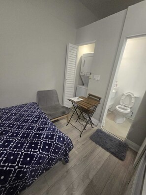 A compact room with a bed, a chair, a small table, and a bathroom.