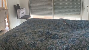 Une chambre avec un grand lit, un luminaire suspendu, une porte coulissante à motifs géométriques et une petite étagère sur laquelle se trouvent un sac et une boîte.