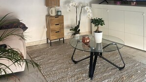 Un salon avec une table basse en verre, un meuble en bois, un canapé blanc et un téléviseur fixé au mur.