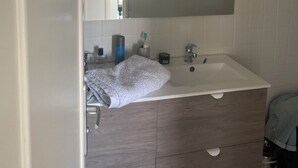 Une salle de bain avec un lavabo blanc, un miroir au-dessus et une serviette accrochée au mur.