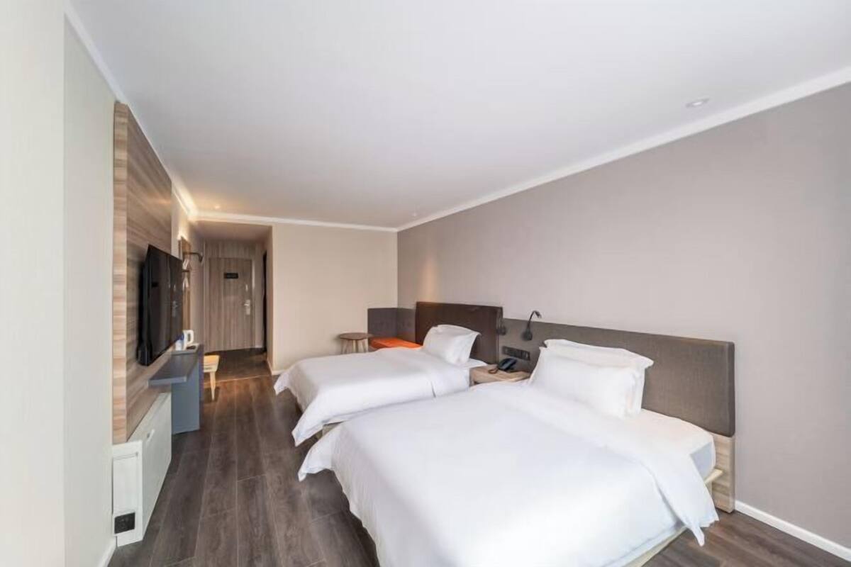 A hotel room with two beds, a TV, a desk, and a bathroom.
