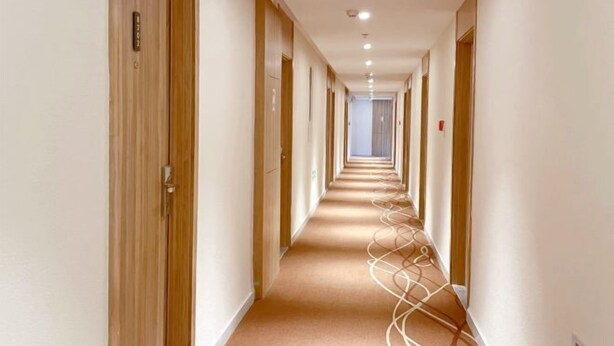 Un long couloir étroit, avec des portes en bois d’un côté et une moquette à motifs de l’autre.