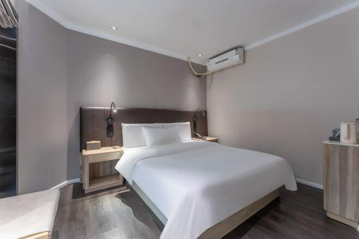 A modern hotel room with a large bed, a bedside table, a nightstand, a wardrobe, and an air conditioning unit.