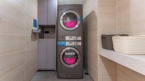 Un lavadero moderno y funcional con dos lavadoras apiladas, un armario pequeño y un estante con cestas.