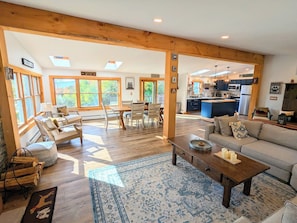 A spacious living area with a wooden ceiling, large windows, a dining table, and a kitchen in the background. - Charming 3BR house, nestled in mountains, pet friendly, 20 minutes from skiing! (Stamford)