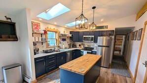 Une cuisine moderne dotée d’un îlot central, de meubles de couleur sombre, d’appareils électroménagers en acier inoxydable et d’une lucarne.
