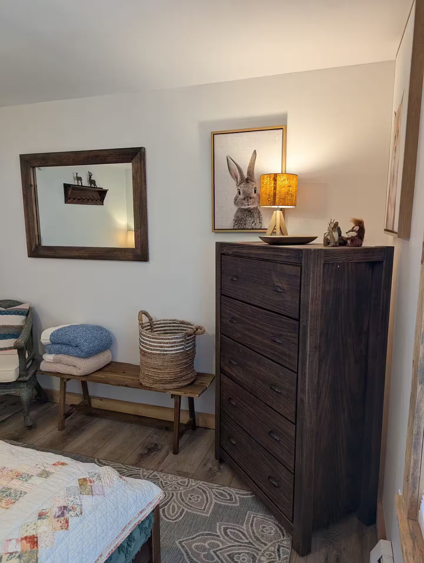 Een slaapkamer met een bed, een kaptafel, een bankje, een lamp en een lijst met een konijn erop.