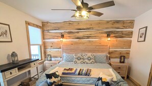 Une chambre à coucher avec un lit, un canapé bleu, une tête de lit en bois, un ventilateur de plafond et une table de chevet.