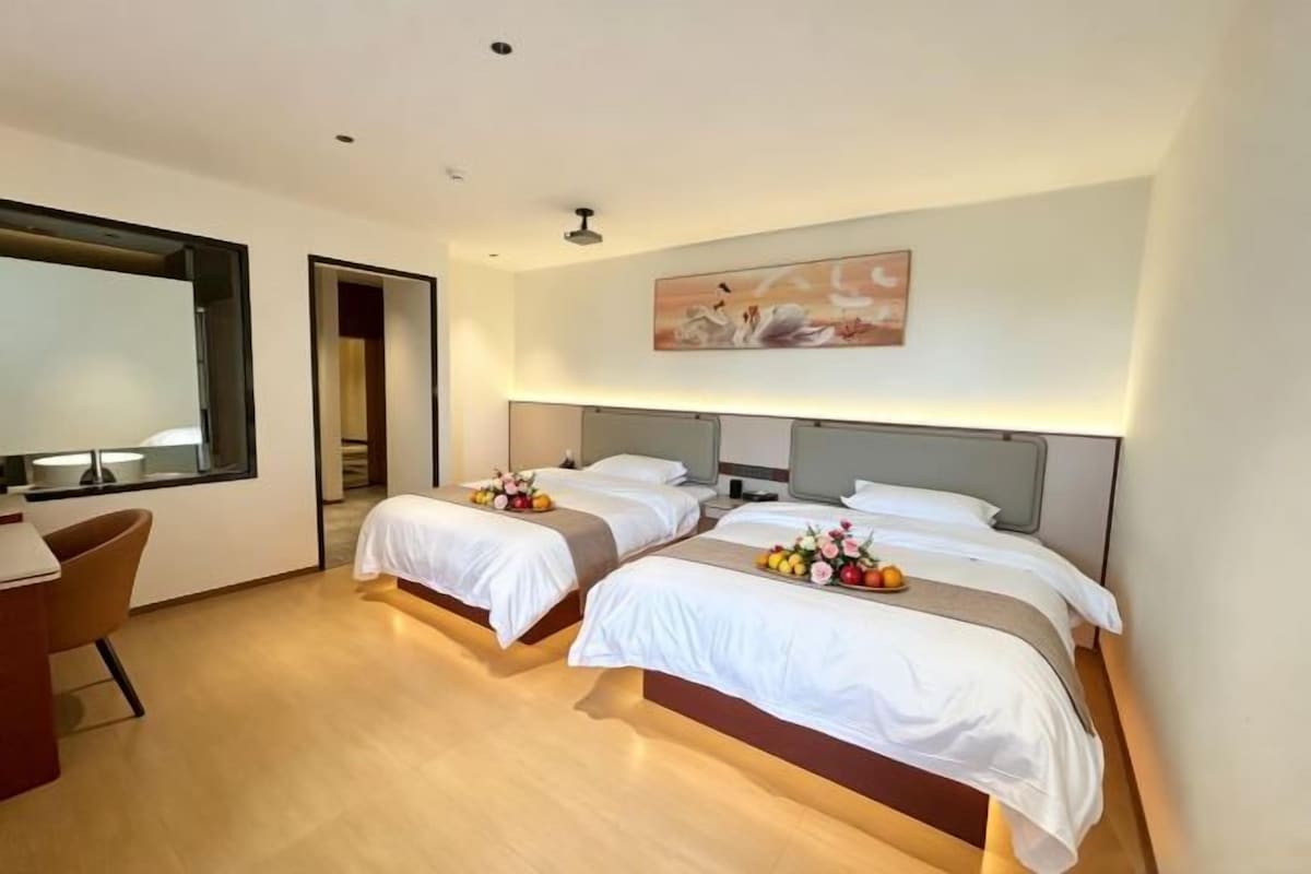 Une chambre d’hôtel avec deux lits, un bureau et un grand miroir.