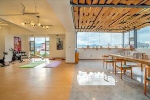 Una habitación amplia con techo de madera, ventanas grandes, equipo de ejercicio y un comedor.