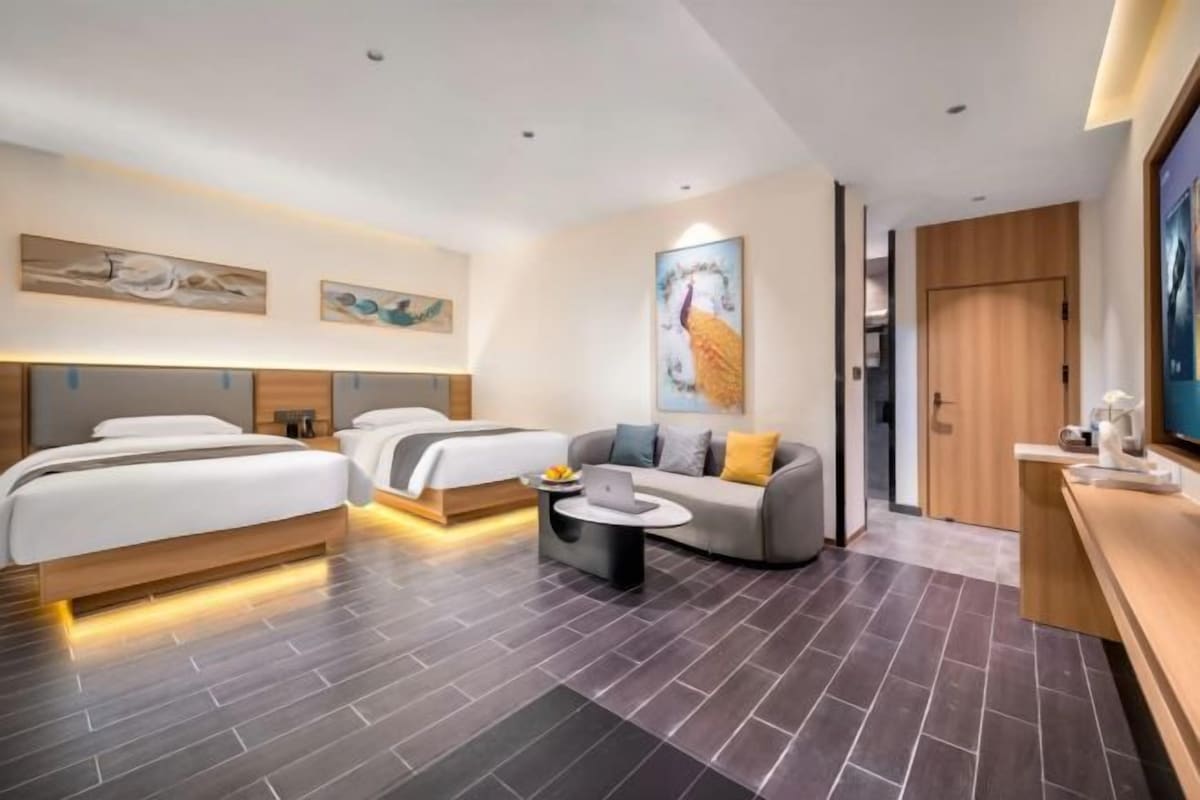 Une chambre d’hôtel avec deux lits, un canapé, une table basse et des œuvres d’art accrochées aux murs.