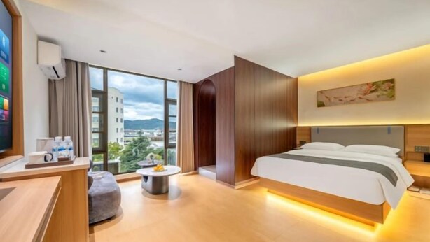 A modern hotel room with a large bed, a desk, a round coffee table, and a view of the city. - Lijiang Yueyou International Hotel (Lijiang Old Town Branch (Lijiang)