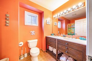 Bathroom features a large mirror with lights, a sink, wooden cabinets, and a toilet.