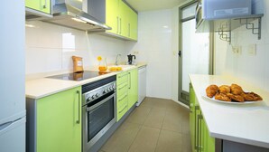 Cocina compacta con armarios verdes, horno de acero inoxidable y encimera blanca.