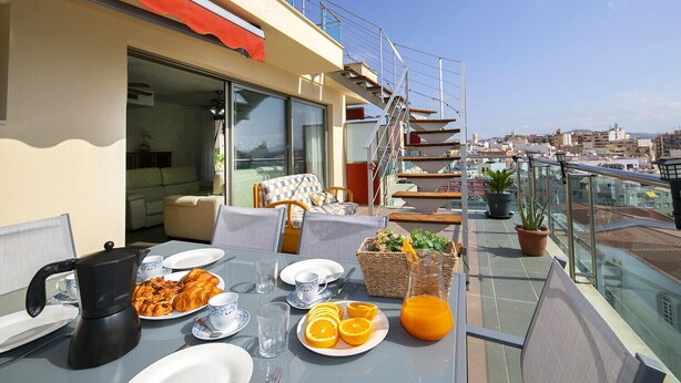 Terraza en la azotea con una mesa lista para el desayuno, con cruasanes, rodajas de naranja y una jarra de zumo de naranja.
