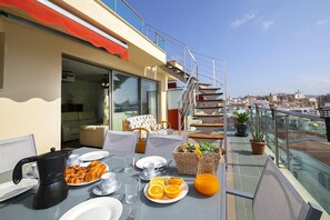 A rooftop terrace with a dining table set for breakfast, including croissants, orange slices, and a pitcher of orange juice. - ATICO BORUMBOT VISTA PISCINA (Calpe)