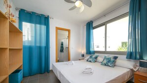 Habitación de hotel con una cama grande, ducha, estante de madera y ventana con cortinas.