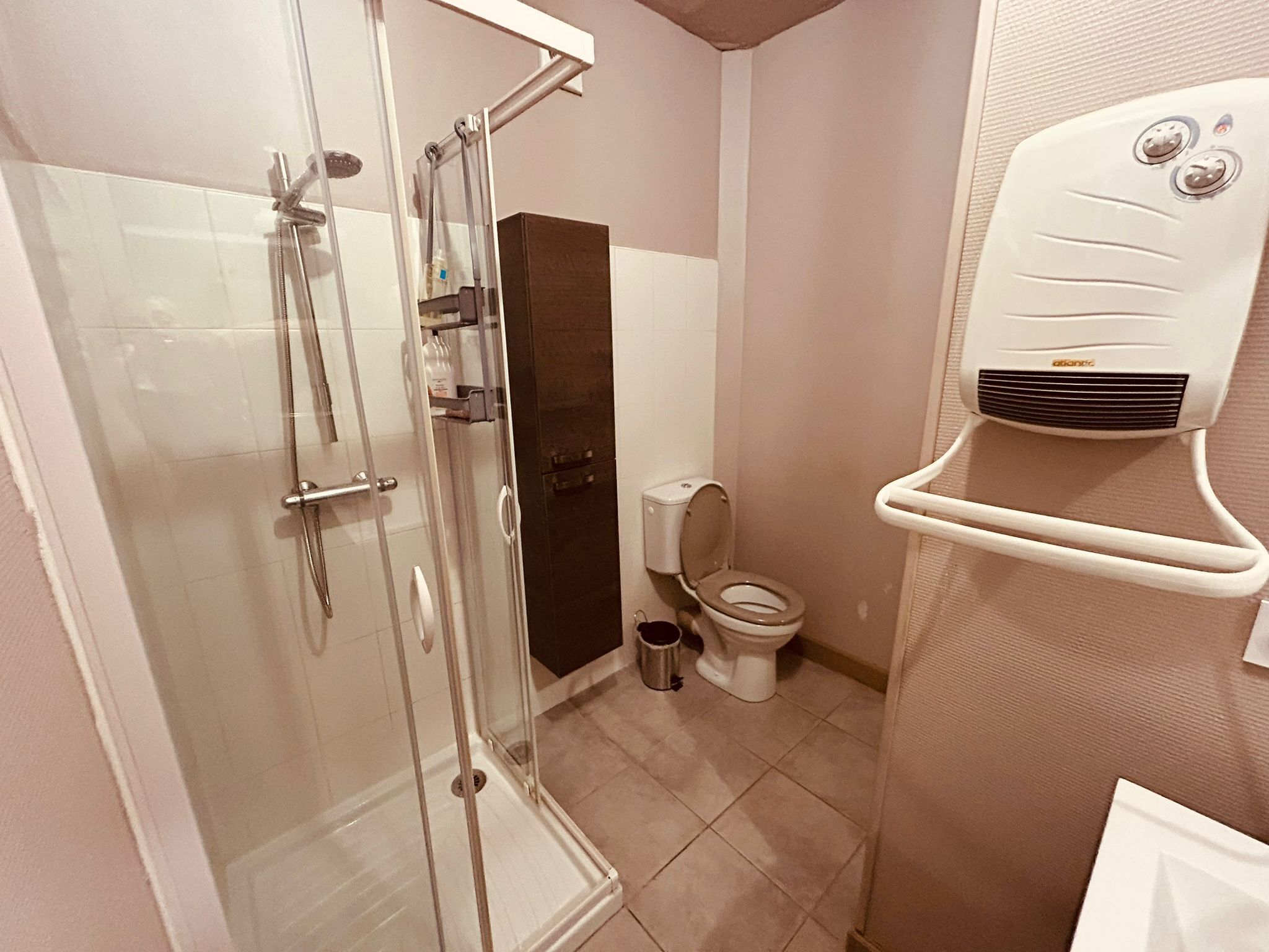 A bathroom with a glass-enclosed shower, a toilet, and a white wall-mounted air purifier.