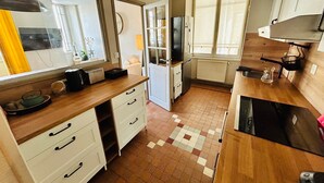 A compact kitchen with white cabinets, a wooden countertop, a tiled floor, and a large window providing natural light. - Large, comfortable apartment right in the center of town, ideal for families. (Villefranche-de-Rouergue)