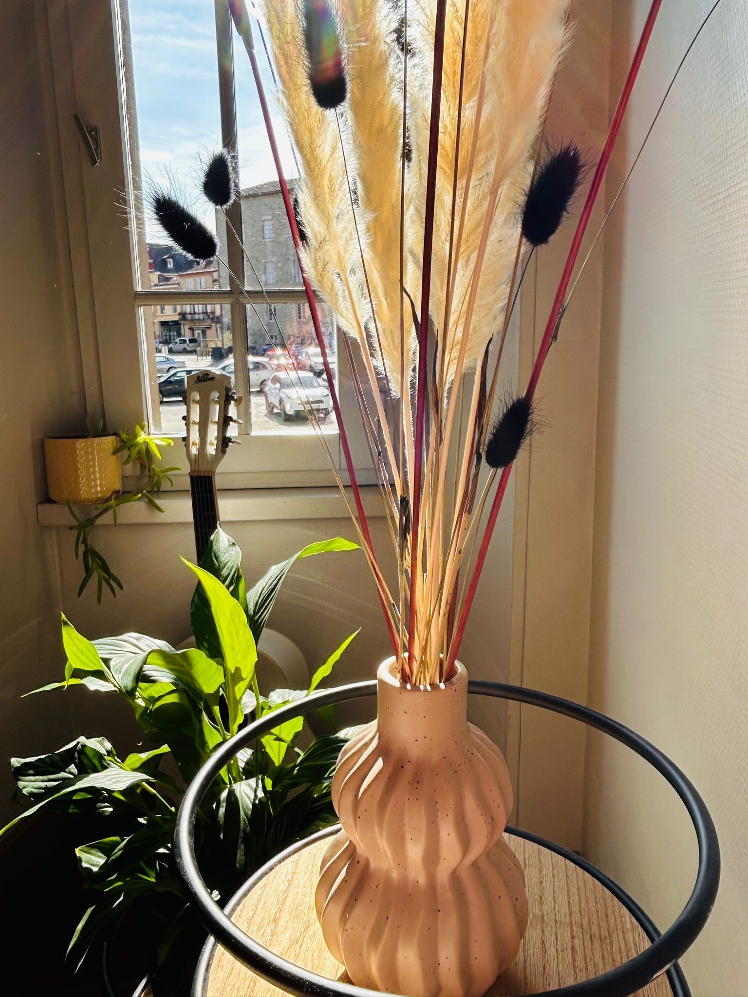 Eine Vase mit Pampasgras auf einem Tisch in der Nähe eines Fensters.