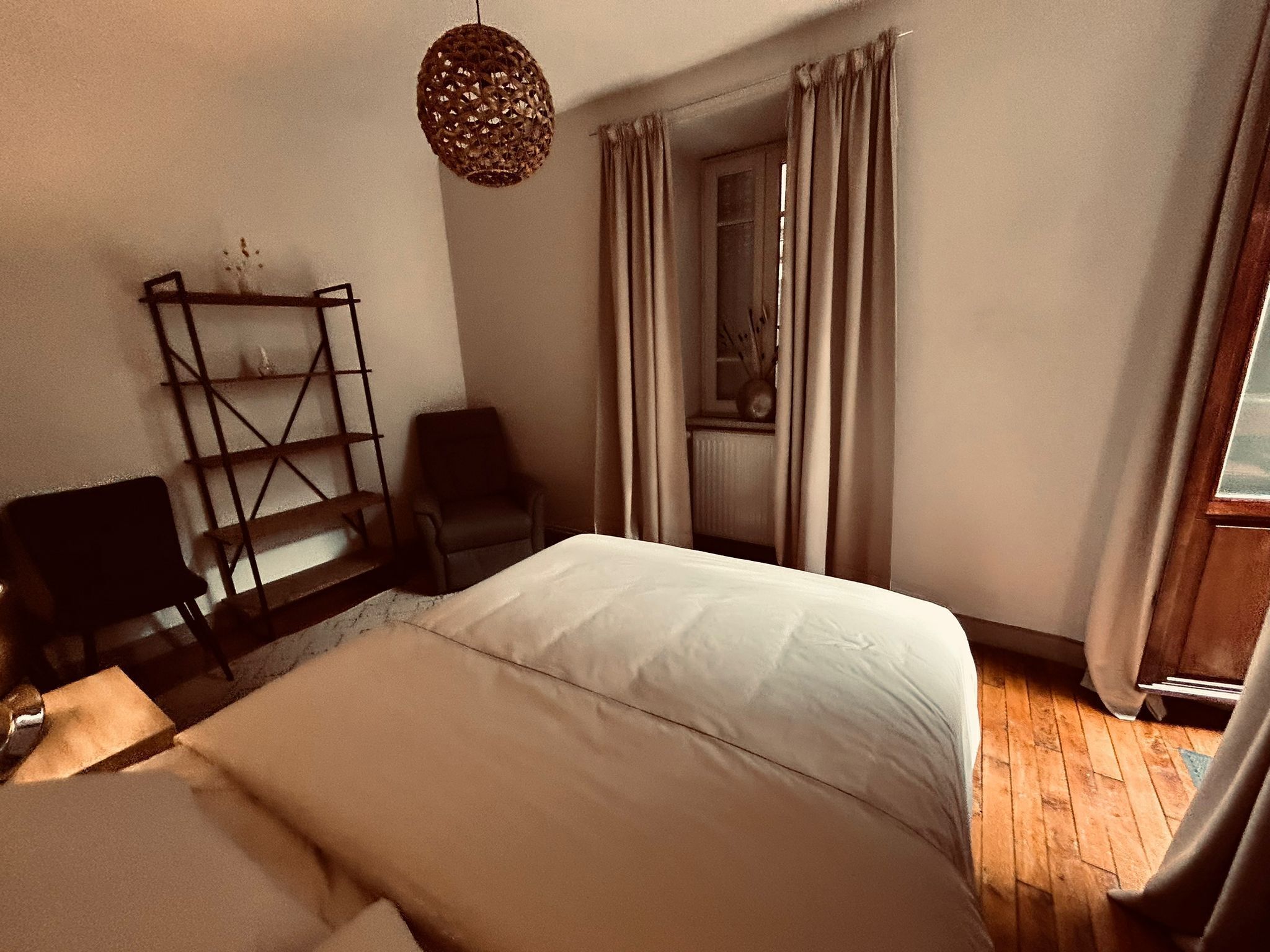 Ein Schlafzimmer mit Bett, Stuhl, Ablagefläche und einer Pendelleuchte.